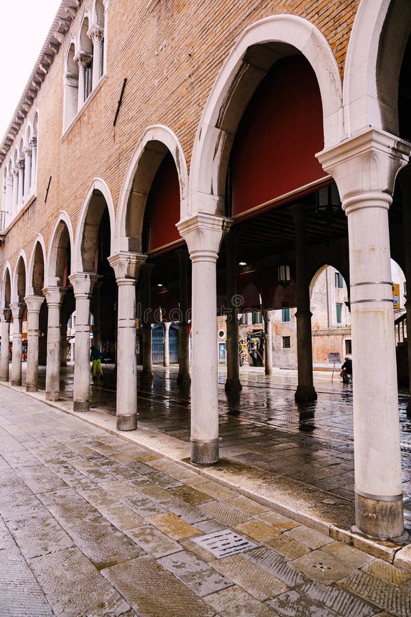 A building in Venice standing on columns. Stone wall of brown brick, white columns and high arches, ancient paving tile. royalty free stock images